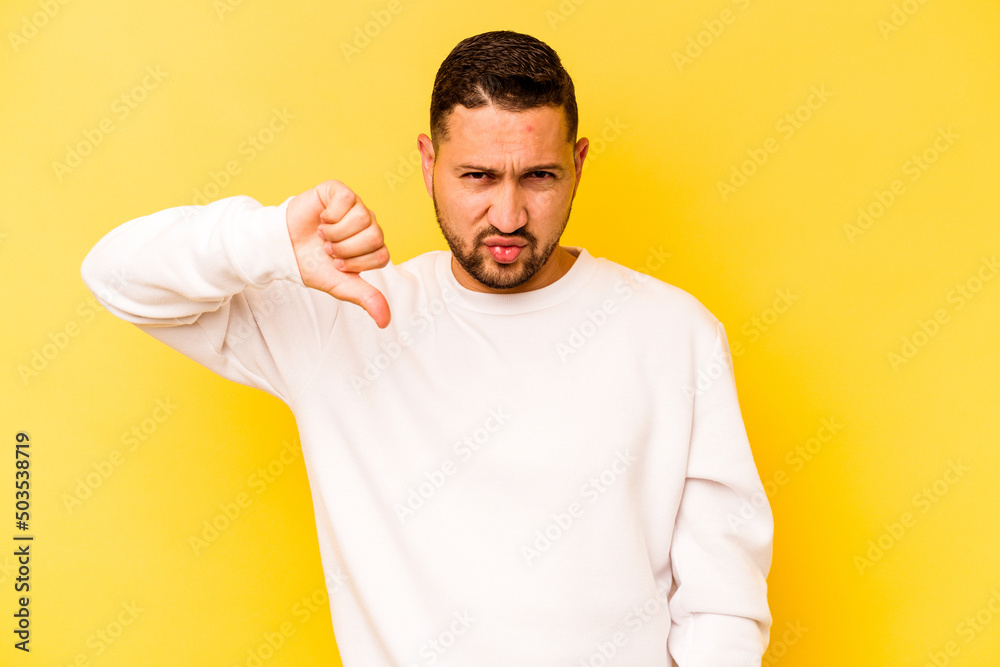 Young hispanic man isolated on yellow background showing thumb down, disappointment concept. Young hispanic man isolated on yellow background showing thumb down, disappointment concept.