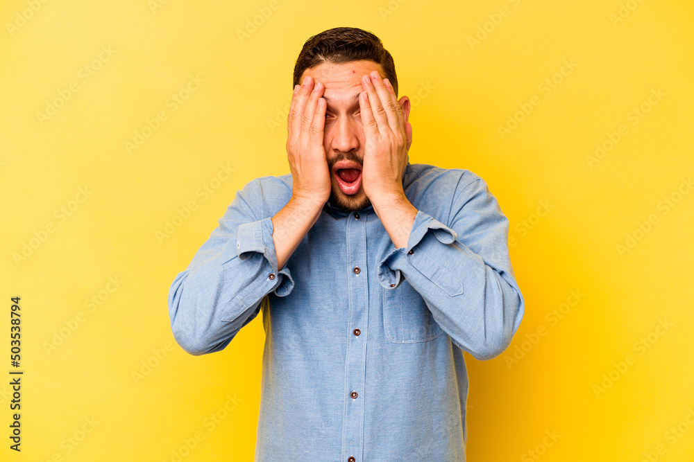 Young hispanic man isolated on yellow background having fun covering half of face with palm. Young hispanic man isolated on yellow background having fun covering half of face with palm.