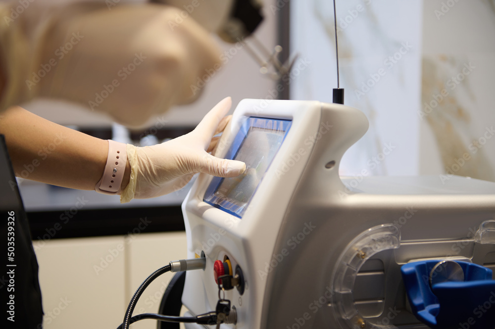 Close-up of beauty therapist hands holding laser resurfacing machine, pointing with finger at the monitor screen, adjusting programs on hardware beauty apparatus Close-up of beauty therapist hands holding laser resurfacing machine, pointing with finger at the monitor screen, adjusting programs on hardware beauty apparatus