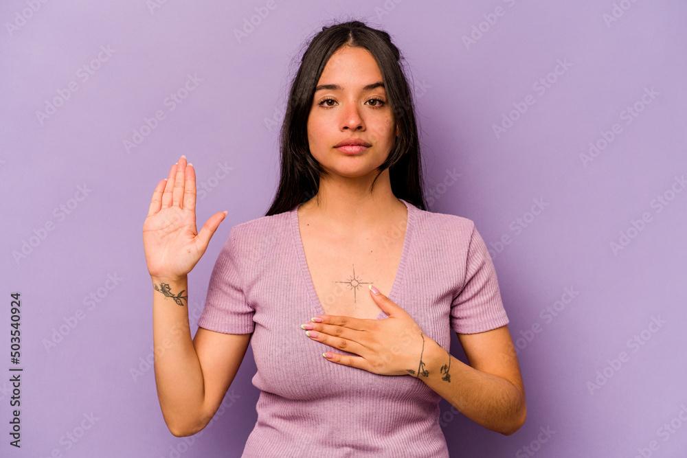 Obraz premium Young hispanic woman isolated on purple background taking an oath, putting hand on chest.