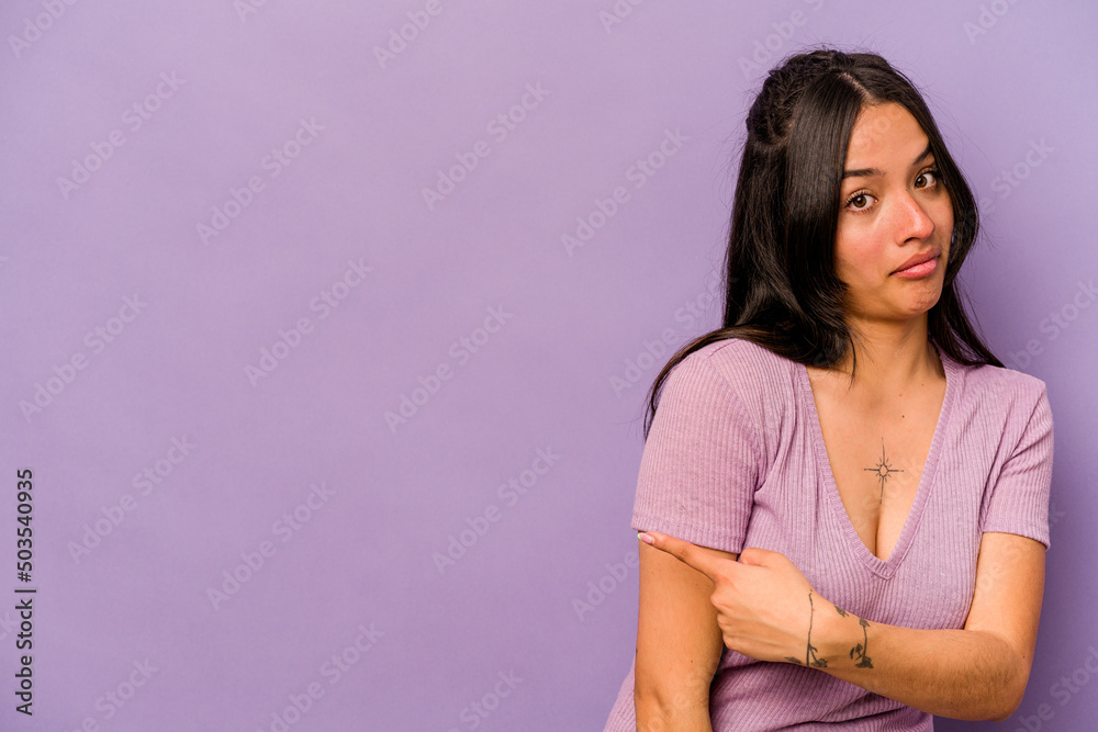 Young hispanic woman isolated on purple background smiling and pointing aside, showing something at blank space. Young hispanic woman isolated on purple background smiling and pointing aside, showing something at blank space.