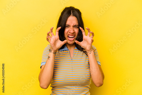 Young hispanic woman isolated on yellow background showing claws imitating a cat, aggressive gesture.