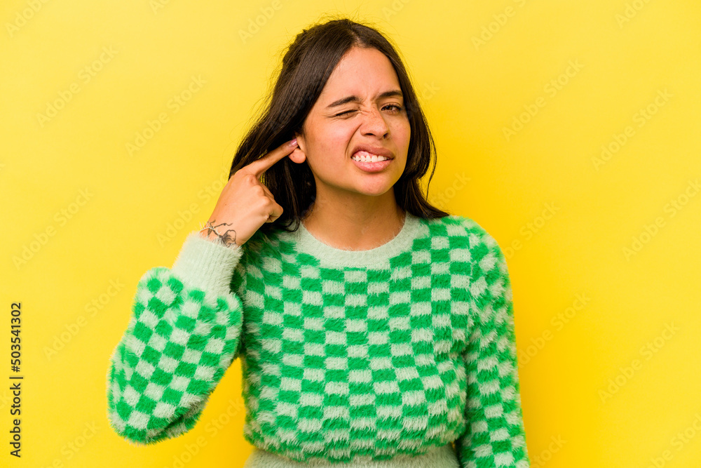 Young hispanic woman isolated on yellow background covering ears with fingers, stressed and desperate by a loudly ambient. Young hispanic woman isolated on yellow background covering ears with fingers, stressed and desperate by a loudly ambient.