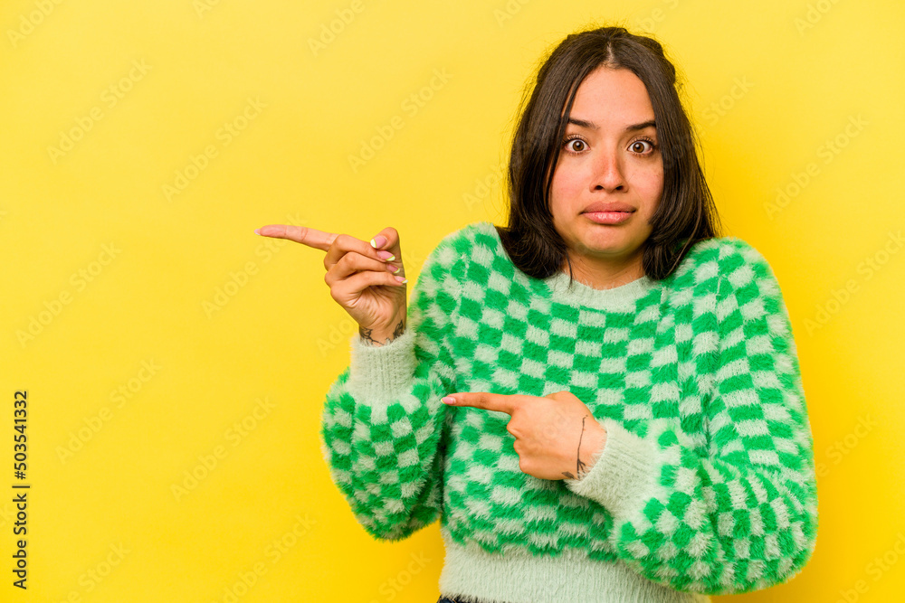 Young hispanic woman isolated on yellow background shocked pointing with index fingers to a copy space.