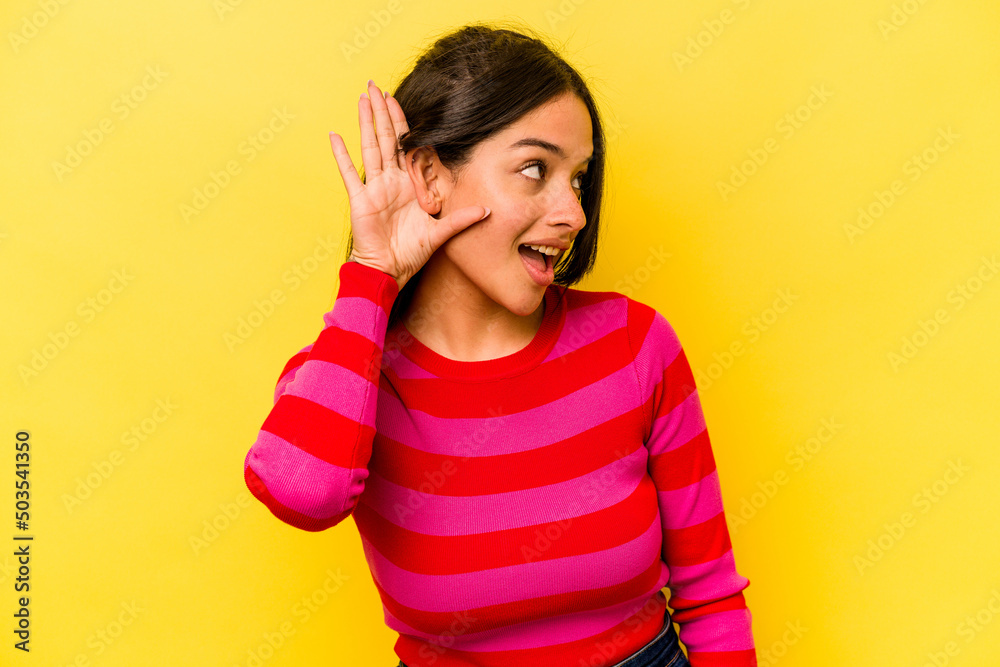 Young hispanic woman isolated on yellow background trying to listening a gossip.