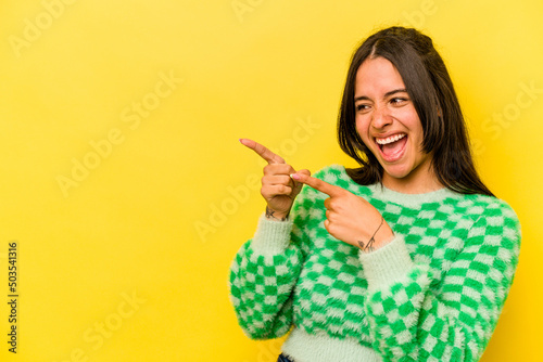Young hispanic woman isolated on yellow background points with thumb finger away  laughing and carefree.