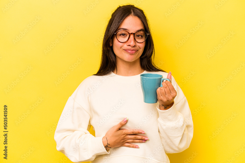 Young hispanic woman holding a mug isolated on yellow background Young hispanic woman holding a mug isolated on yellow background