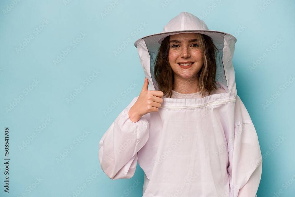Young caucasian beekeeper woman isolated on blue background smiling and raising thumb up Young caucasian beekeeper woman isolated on blue background smiling and raising thumb up