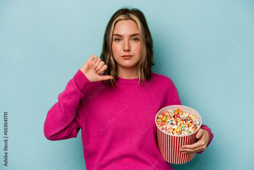 Young caucasian woman holding popcorn isolated on blue background showing a dislike gesture, thumbs down. Disagreement concept.