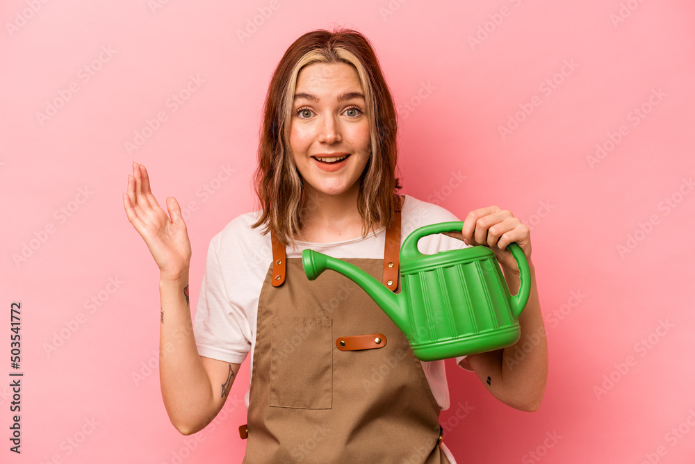 Young gardener woman holding watering can isolated on pink background receiving a pleasant surprise, excited and raising hands. Young gardener woman holding watering can isolated on pink background receiving a pleasant surprise, excited and raising hands.