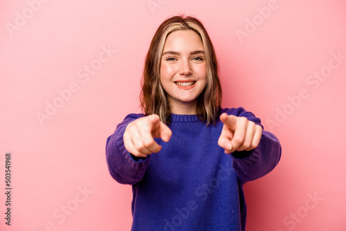 Foto Young caucasian woman isolated on pink background cheerful smiles pointing to front