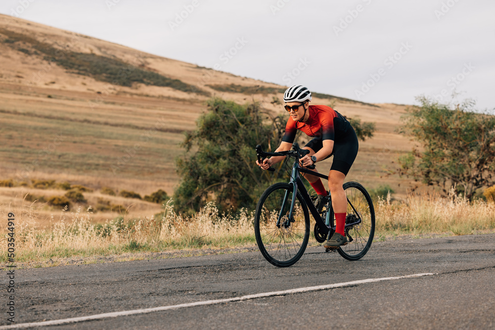 Athletic woman taking a bicycle ride on the empty countryside road. Professional cyclist practicing outdoors.