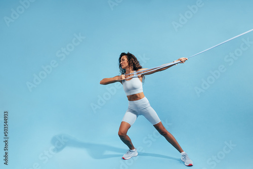 Muscular woman pulling resistance band. Young female in sportswear doing intense exercises with elastic band. © Artem Varnitsin