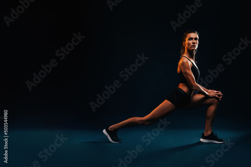 Side view of fit woman stretching legs. Caucasian female working out on black background.