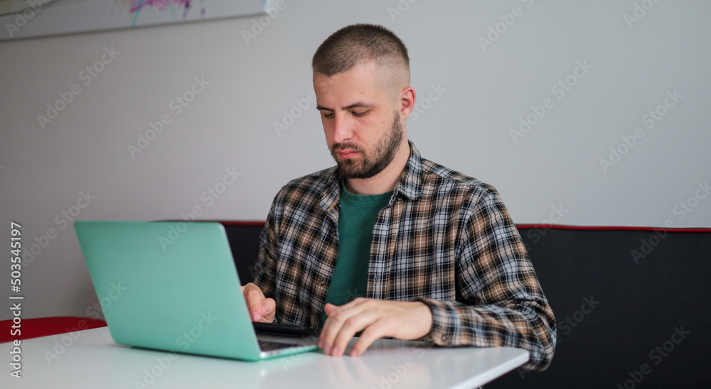 The guy in the shirt is working on the computer, working remotely. Freelancer. The guy in the shirt is working on the computer, working remotely. Freelancer.