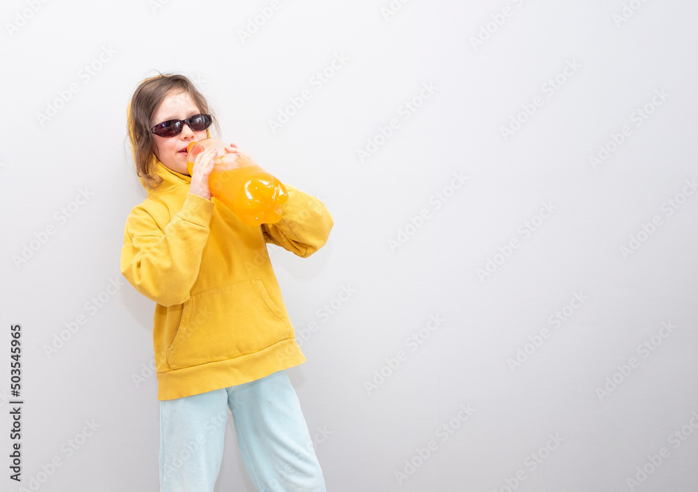 Child, Caucasian 6 years old, in a yellow sweatshirt with a hood on a gray background. The child rejoices and gesture holds a bottle of lemonade in his hands. Child, Caucasian 6 years old, in a yellow sweatshirt with a hood on a gray background. The child rejoices and gesture holds a bottle of lemonade in his hands.