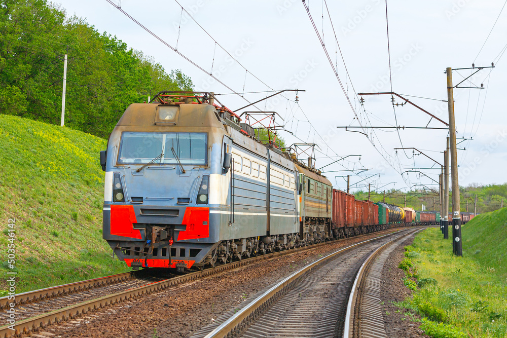 Four powerful electric locomotives pull a long heavy train to the sorting station. Spring evening lighting.