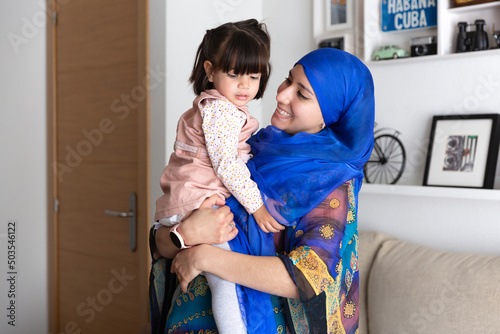 Young Muslim woman with her daughter in her arms. Single parent family at home.