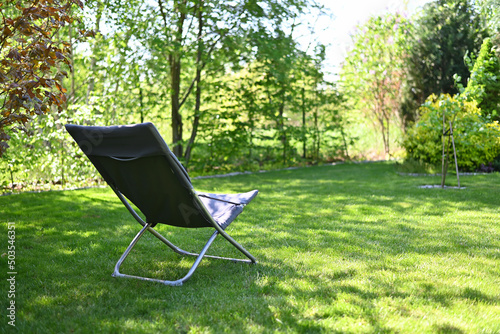 Folding chair surrounded by green leaves in a garden. Relaxation in the garden. Cottage aesthetics. Vacation outside the city. Warm summer day. 