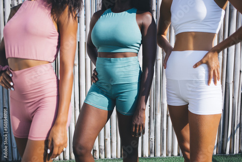 Cropped female athletes in trendy tracksuits posing during workout teamwork outdoors - reaching body positive lifestyle and vitality, unrecognizable multiracial fit girls in sportswear outdoors