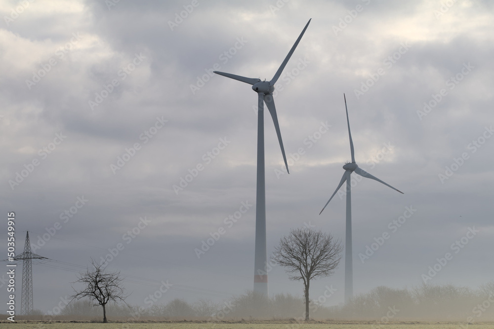 Windkraftanlagen im Nebel mit Bäumen und Wolken am Himmel Windkraftanlagen im Nebel mit Bäumen und Wolken am Himmel