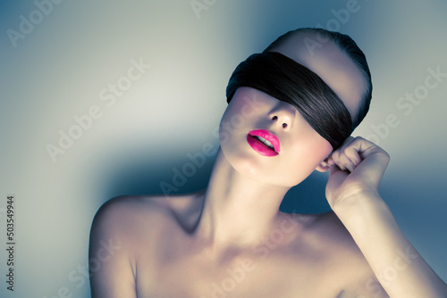 Dramatic Portrait of a Young Brunette Woman Covering her Eyes with a Blindfold made out of her own Hair and Hot Pink Lips in Studio