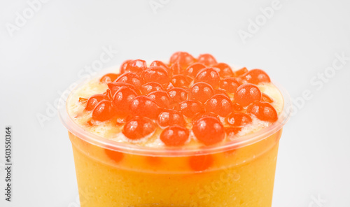 Closeup of a cup of delicious orange bubble tea with boba on top of it on a white background photo