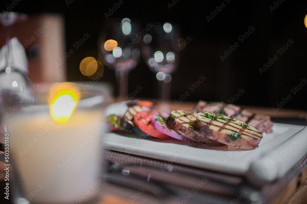 A plate of grilled beef meat with grilled slices of potatoes, tomatoes and onions