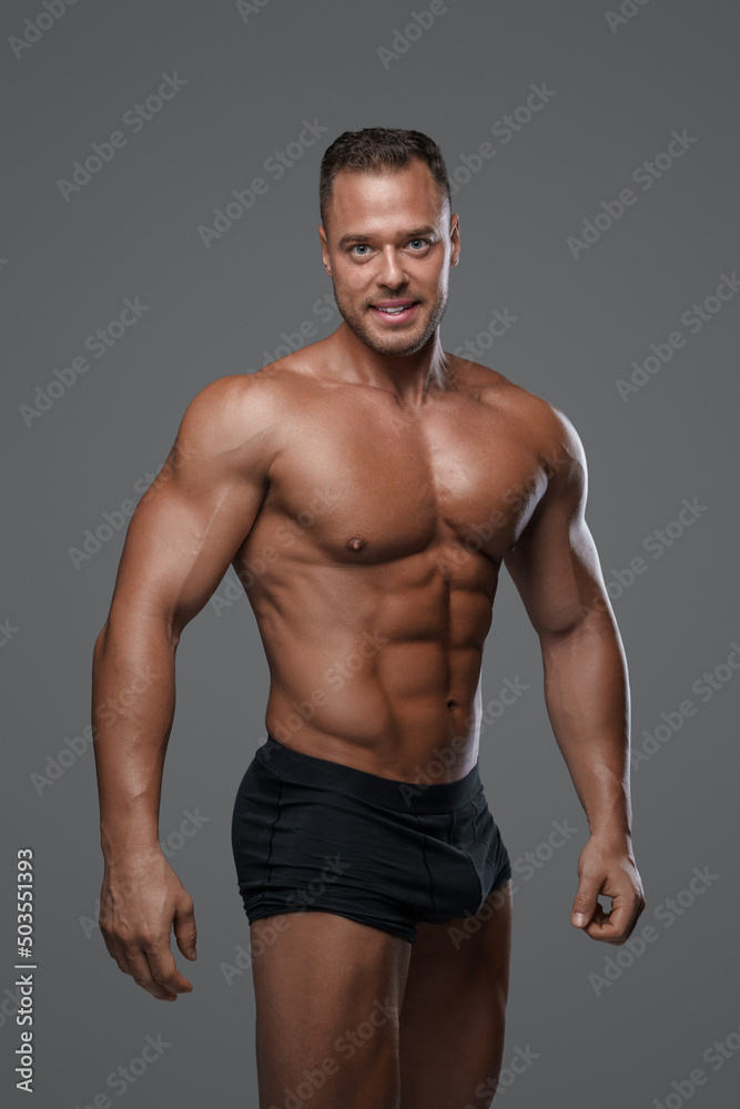 Tanned athlete with naked body and short hairstyle posing against gray background.