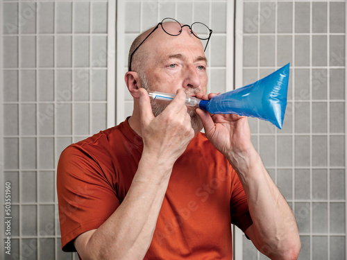 Head and shoulders portrait of a senior man performing breath test to diagnose SIBO (small intestinal bacterial overgrowth)
