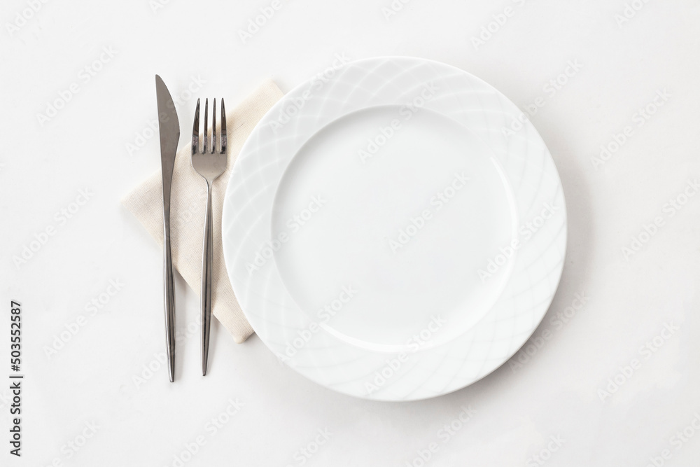 Empty white plate with fabric napkin, a fork and a knife on white table. Top view. Empty white plate with fabric napkin, a fork and a knife on white table. Top view.