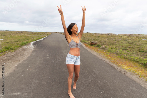 African American woman with long black hair raising her arms outside on country road