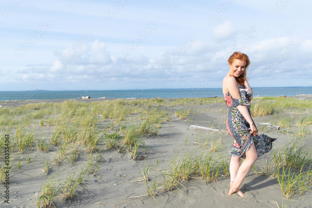 Redhead woman with freckles wearing dress at ocean beach.