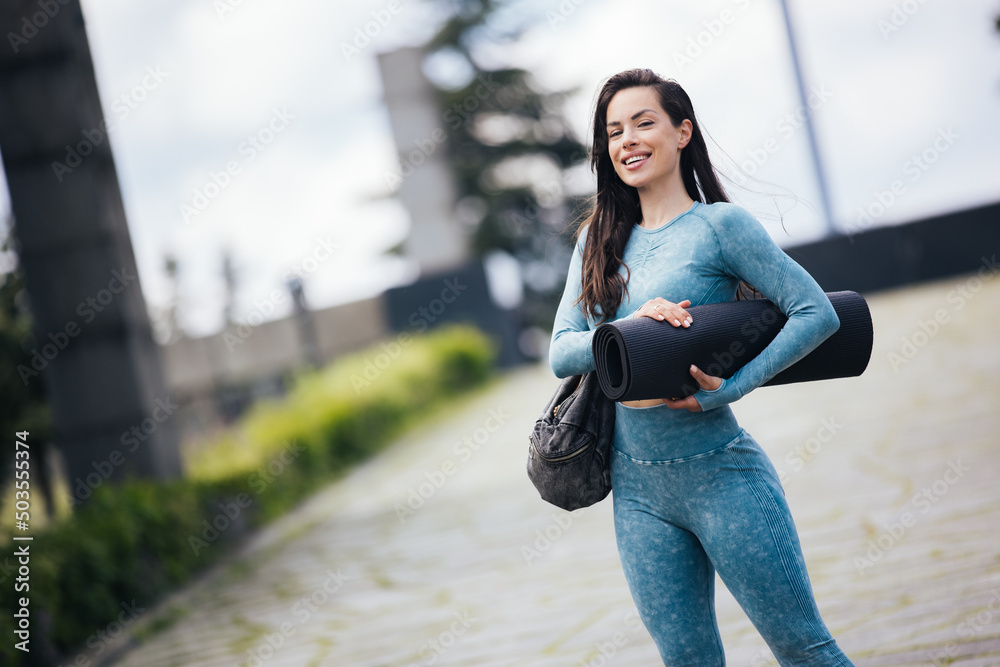 Ready for training. Fit woman in a blue sportswear carrying bag with roll mat and going to park for fitness or yoga workout.Fitness lifestyle concept