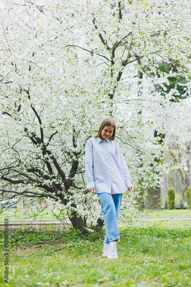 A woman in a white shirt and jeans with glasses in her hands in a spring garden. A woman in a white shirt and jeans with glasses in her hands in a spring garden.