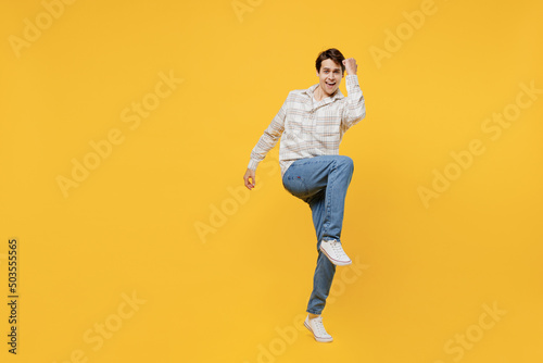Full body young fun smiling happy caucasian man 20s wearing white casual shirt doing winner gesture celebrate clenching fists say yes raise up leg isolated on plain yellow background studio portrait