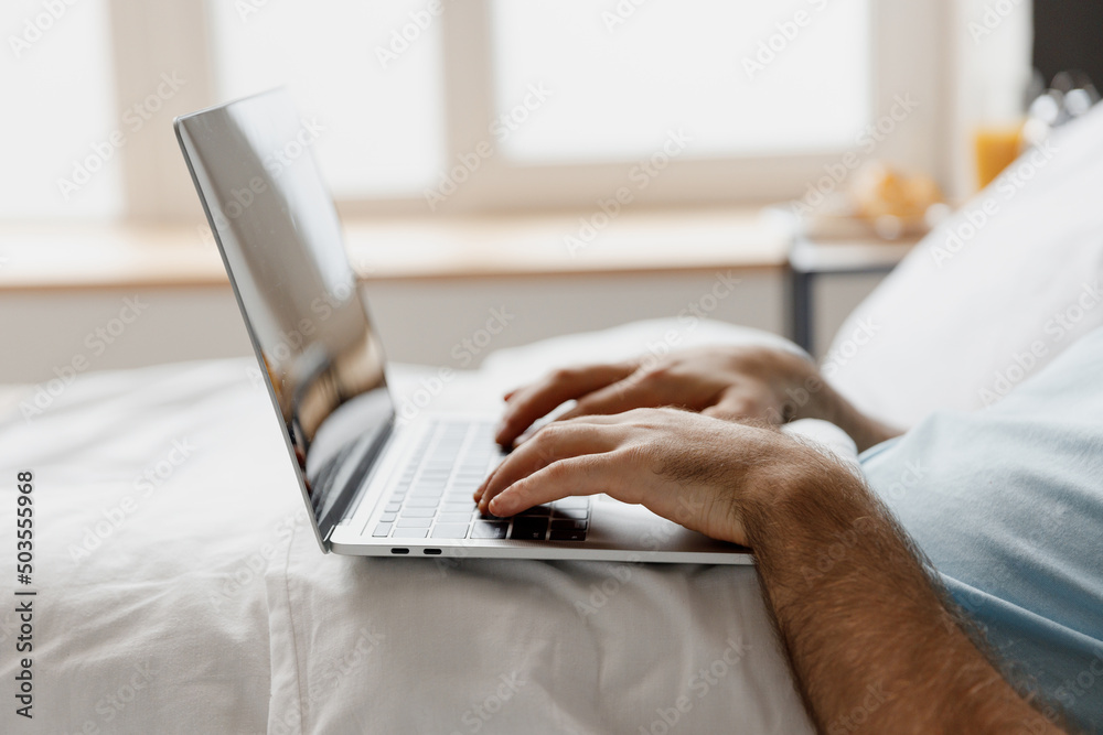 Naklejka premium Close up cropped freelancer man lying in bed hold use working on laptop pc computer typing message rest relax spend time in bedroom lounge home in own room house wake up dream. Remote jobs concept