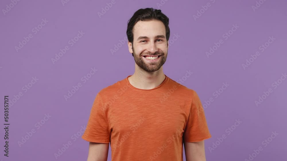 Smiling charming happy young brunet bearded man 20s wears red t-shirt looking camera wink eye blink isolated on plain pastel light purple background studio portrait. People emotions lifestyle concept Smiling charming happy young brunet bearded man 20s wears red t-shirt looking camera wink eye blink isolated on plain pastel light purple background studio portrait. People emotions lifestyle concept