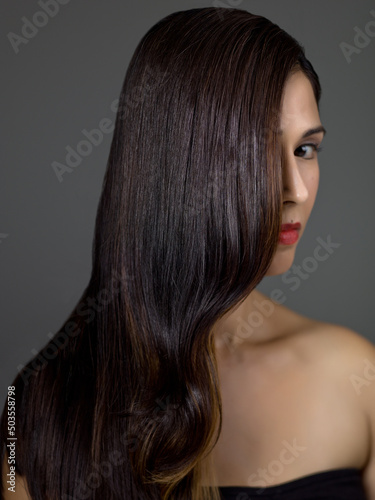 Perfect Long Wavy Hair on a Beautiful Brunette Fashion Model in Studio on a Grey Background