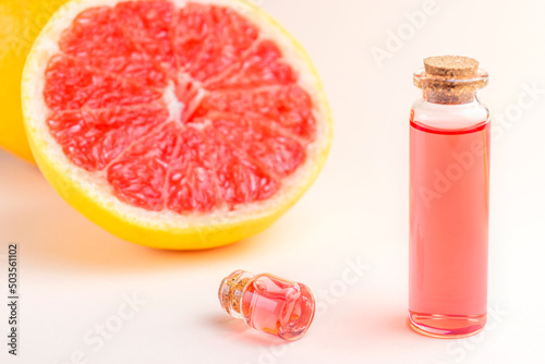 Grapefruit essential oil in glass bottles on pink background with fresh fruit