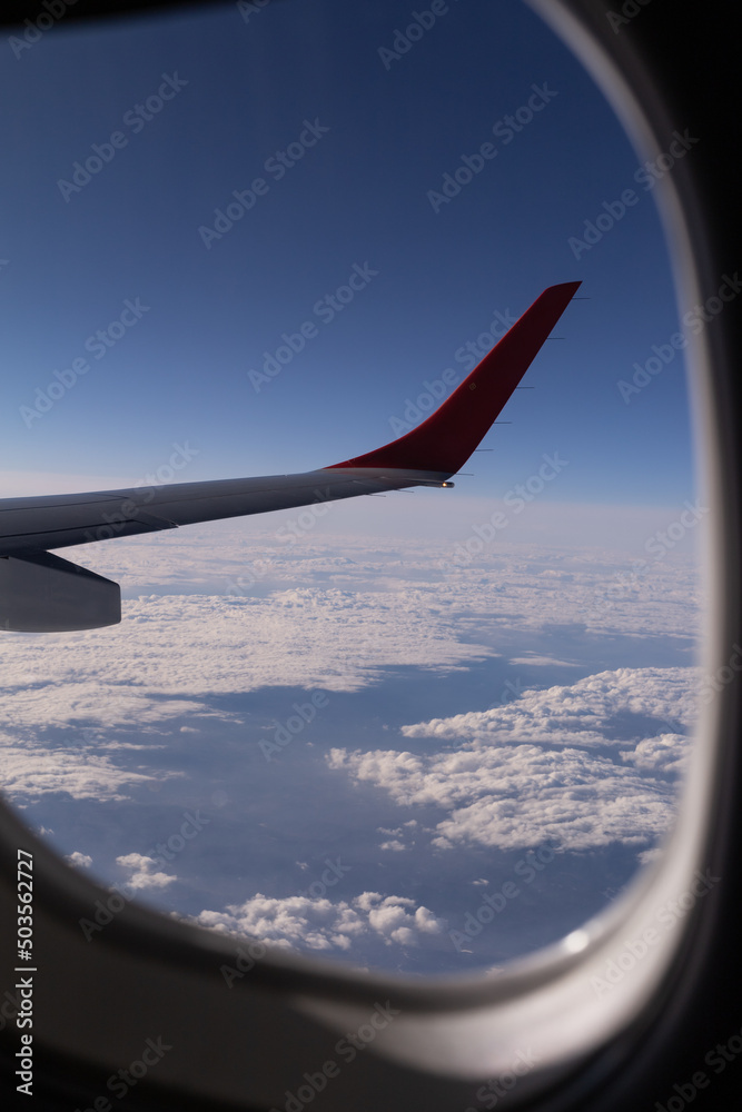 the wing of flying aircraft against background clouds through porthole