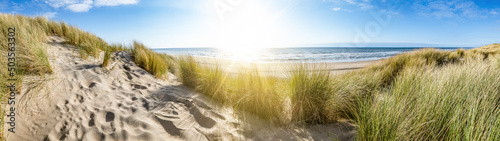 Fototapeta Naklejka Na Ścianę i Meble -  Panoramic landscape background banner panorama of sand dune, beach and ocean North Sea with blue sky, clouds and sunbeams