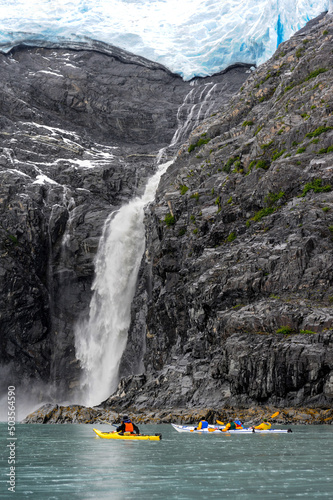 Group of kayaks at bottom of glacier waterfall in the rain, Alaska photo