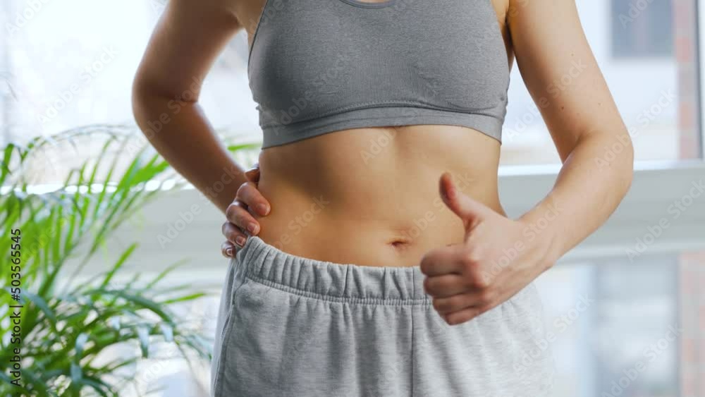 Woman puts on her pants, strokes her stomach and gives a thumbs up. Concept of healthy digestion and bowel function.