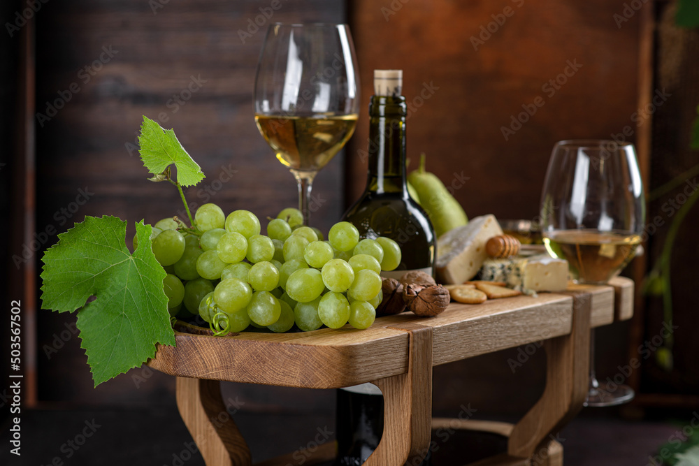 A bottle of wine. Green ripe pear and brie cheese with honey and crackers. Green grapes.