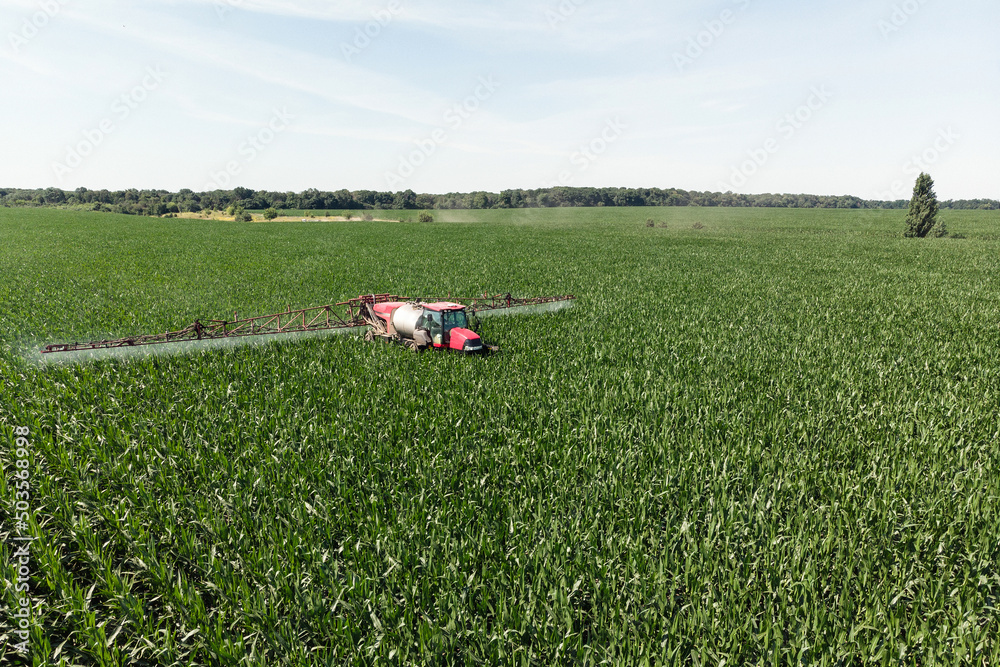 Self-propelled sprayer sprays green corn with pesticides on a photo field from a drone. The tractor sprays the grass with pesticides. Self-propelled sprayer sprays green corn with pesticides on a photo field from a drone. The tractor sprays the grass with pesticides.