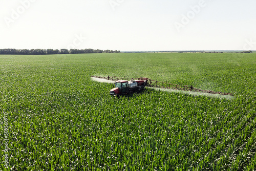 Self-propelled sprayer sprays green corn with pesticides on a photo field from a drone. The tractor sprays the grass with pesticides.
