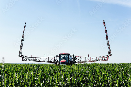 Self-propelled sprayer sprays green corn on the field front view from the side.