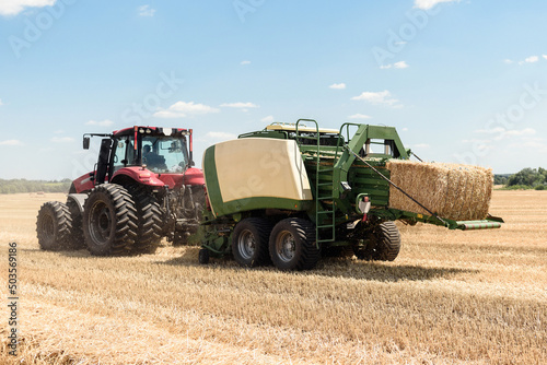 Tractor collects straw in bales on the field. special agricultural machinery. Harvesting hay  straw. Field with bales