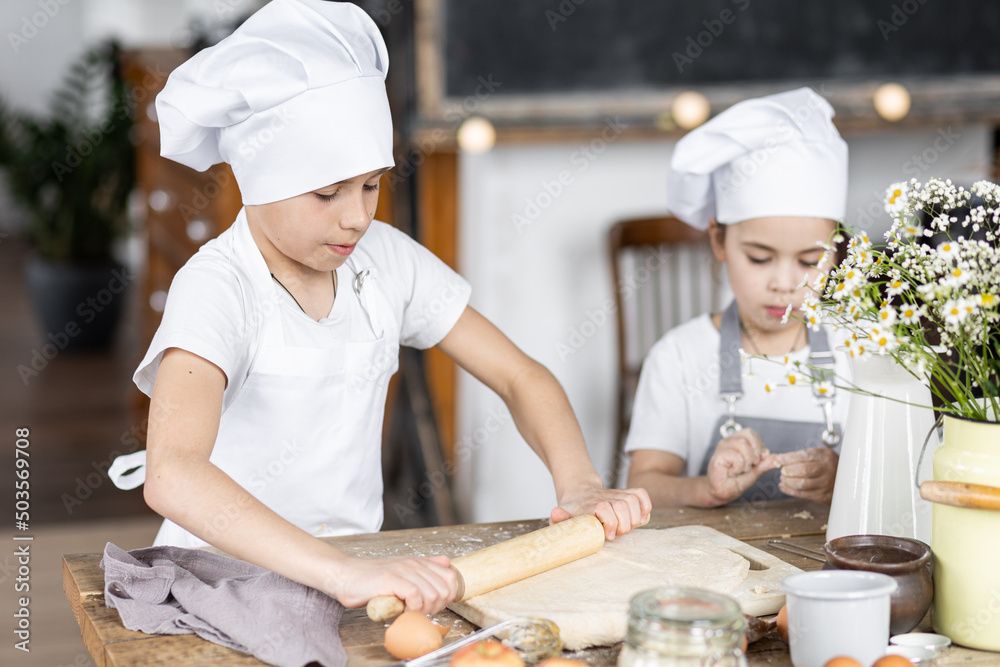 Brother and sister baking homemade sweet pie together, having fun. Home bakery, little kids in process of food preparation in the kitchen at home, helping mother, doing chores